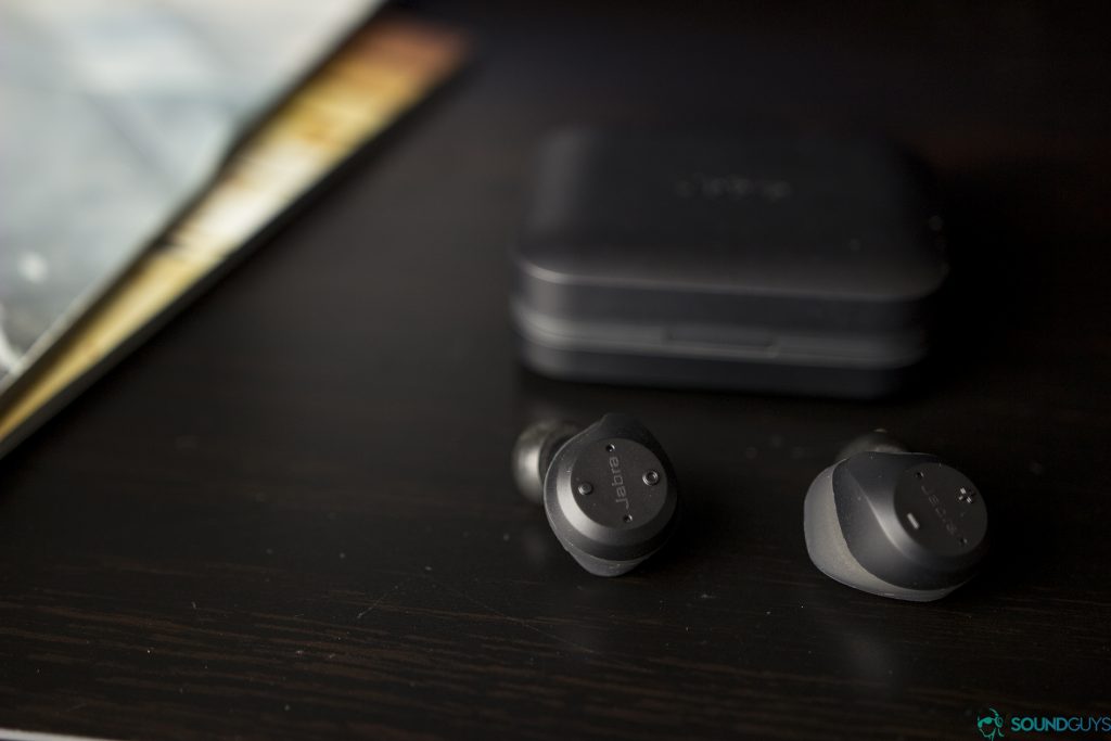 A photo of the Jabra Elite Sport true wireless running earbuds on a wooden surface with the charging case in the background.