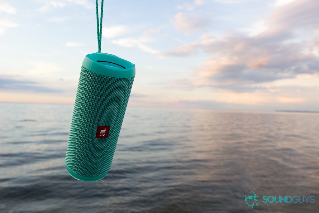 The teal JBL Flip 4 being held up by its string over the water. 