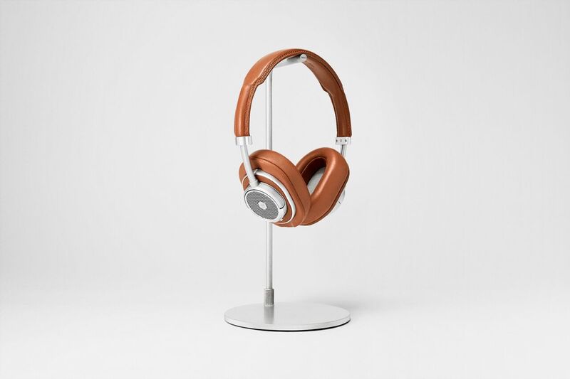 Master & Dynamic MW50+: The brown version of the headphones with the over-ear pads installed. The headphones are on a silver headphone stand against a light-gray background.