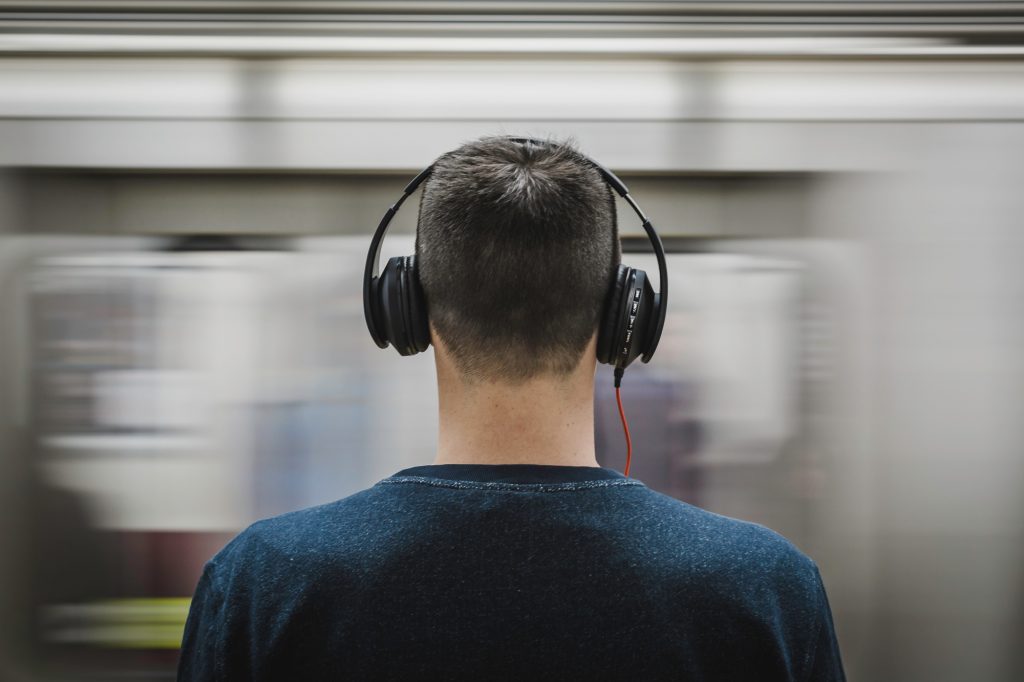 noise cancelling headphones: A photo of a young man wearing headphones in front of a moving train, for the article 