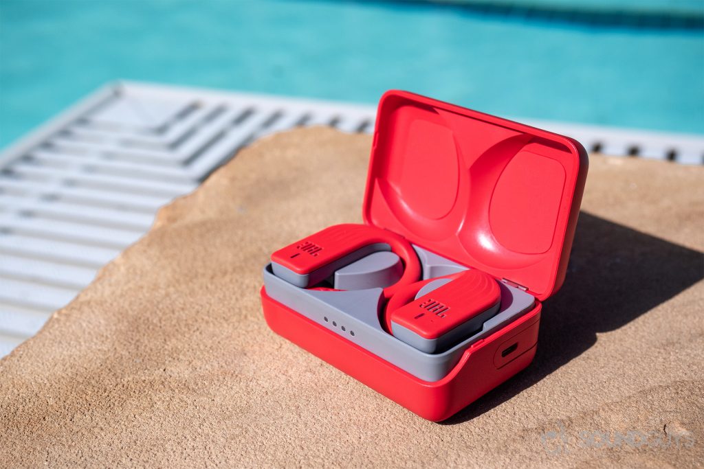 The JBL Endurance Peak earbuds in the case on pool grounds, with a pool in the background.