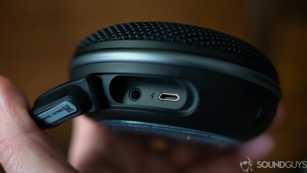 Man holding the JBL Clip 3 with the protective flap open revealing the micro USB and 3.5mm input.