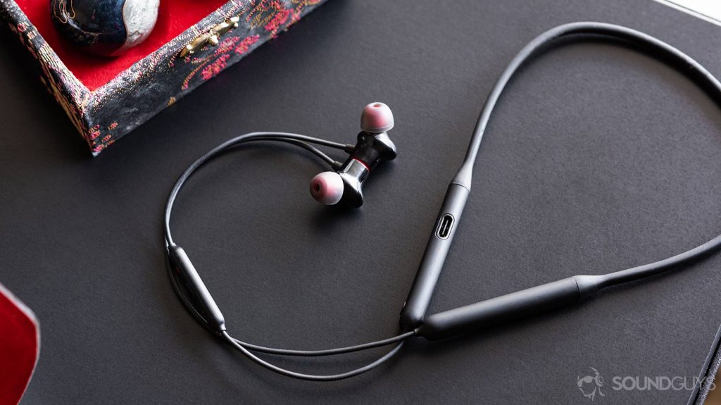 Conference calls - OnePlus Bullets Wireless 2: Full image of the earbuds and neckband with the cable curling up and around on a black table.