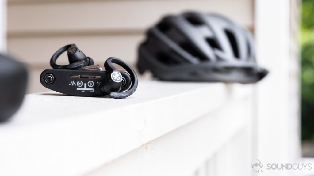 A picture of the JLab JBuds Air Sport, an alternative to the Creative Outlier Gold, resting on a bike tool with a bike helmet in the background.
