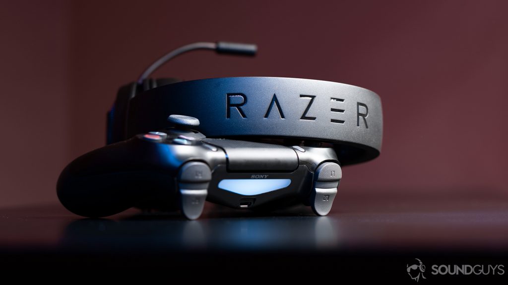 The Razer Kraken cheap gaming headset leaning against a PS4 controller with the headband facing the lens to show the Razer logo.