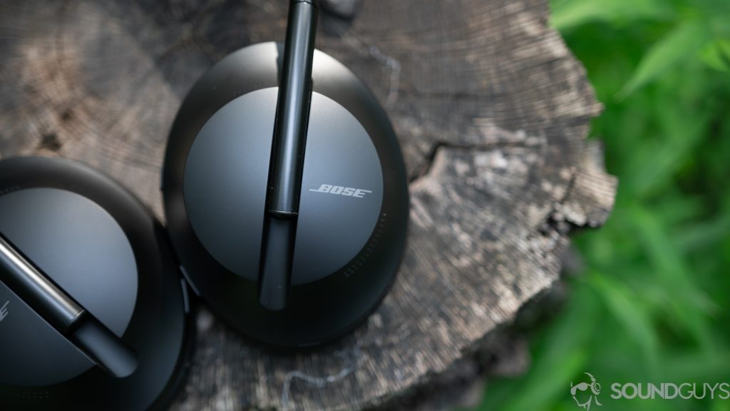 The ear cups of the Bose Noise Cancelling Headphones 700 on top of a tree stump with grass in the background. 