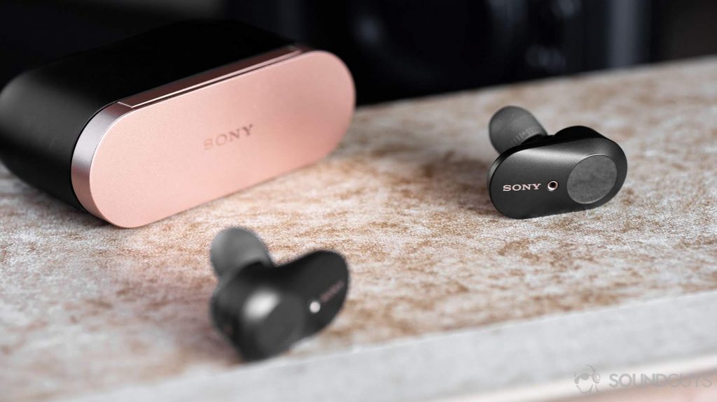 Sony WF-1000XM3 earbuds on a beige book with the closed charging case closed in the background.