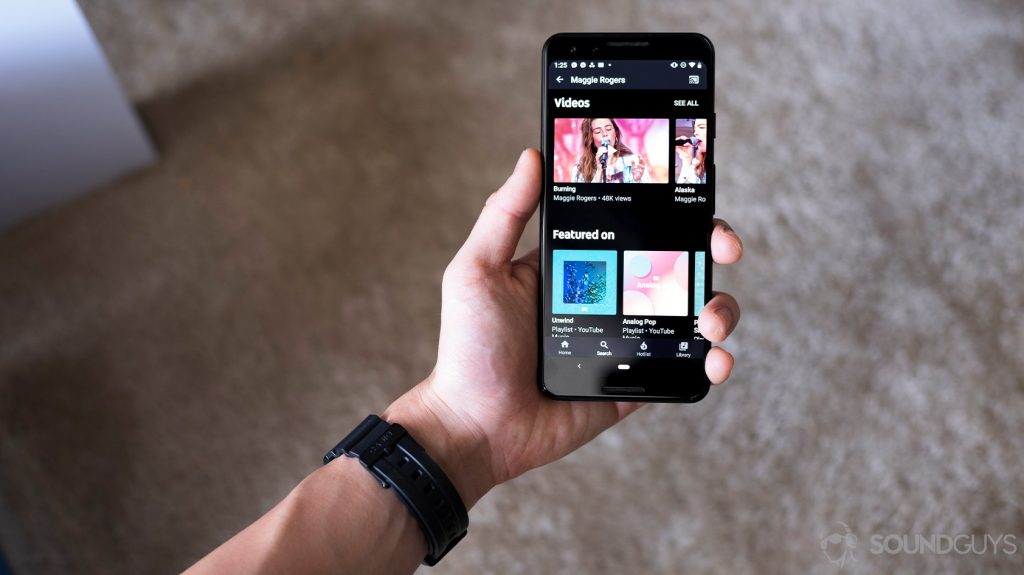 A hand holding a Google Pixel 3 with the YouTube Music Premium app open to search.