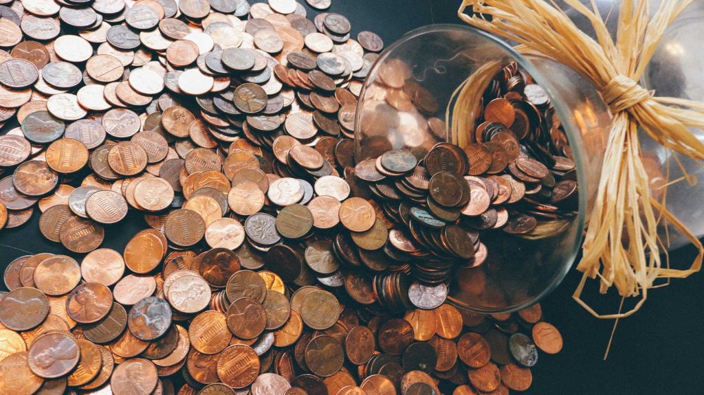 A stock image of pennies spilling onto a table from a glass jar.