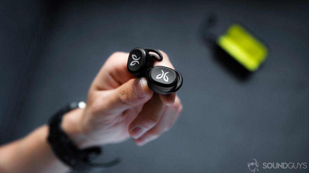 An image of the Jaybird Vista earbuds being held in a hand with the open charging case in the background.