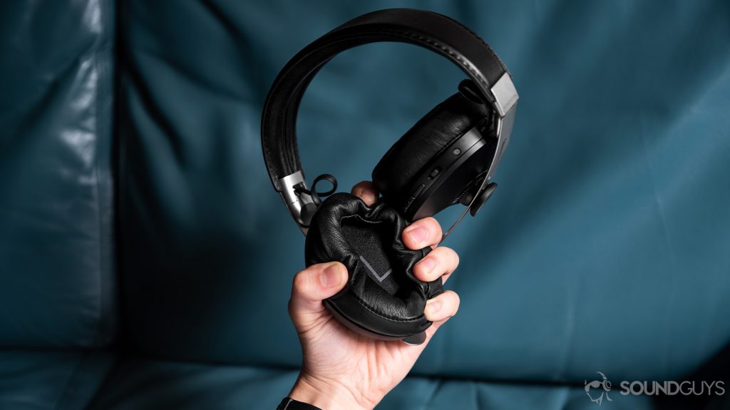 A picture of he Sennheiser Momentum Wireless 3 left ear pad begin crushed in the hand in front of a teal couch.