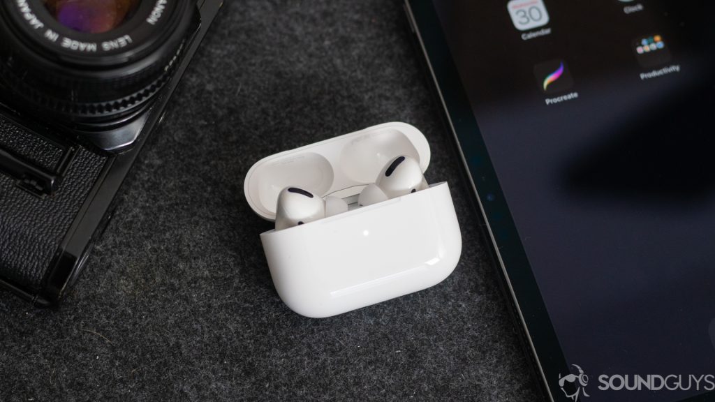 A photo of the AirPods Pro earbuds in the wireless charging case next to an iPhone and digital camera.