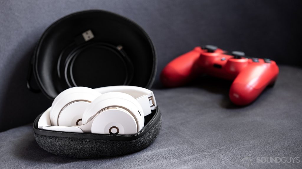 A photo of the Beats Solo Pro on-ear noise cancelling headphones folded in the cloth carrying pouch with the included Lightning cable and a PS4 controller (red) in the background.