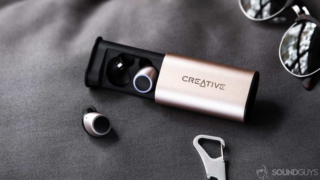 An image of the Creative Outlier Air earbuds, one in the case and one out, with sunglasses in the back right corner.