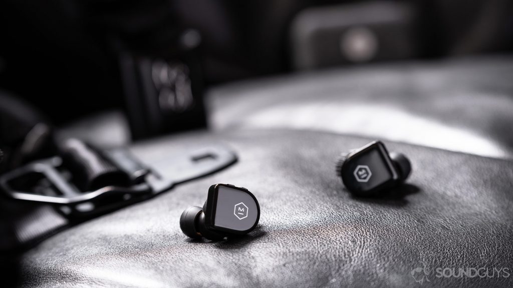 An image of the Master & Dynamic MW07 Go true wireless earbuds on a black leather surface with an out of focus Chrome Industries messenger bag in the background.