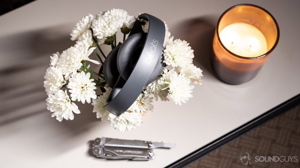A picture of the Beats Solo3 Wirless headphones folded atop a bed of flowers with a candle and multitool.