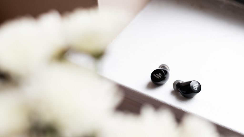 A photo of the Edifier TWS1 true wireless earbuds on a windowsill with flowers in the foreground.