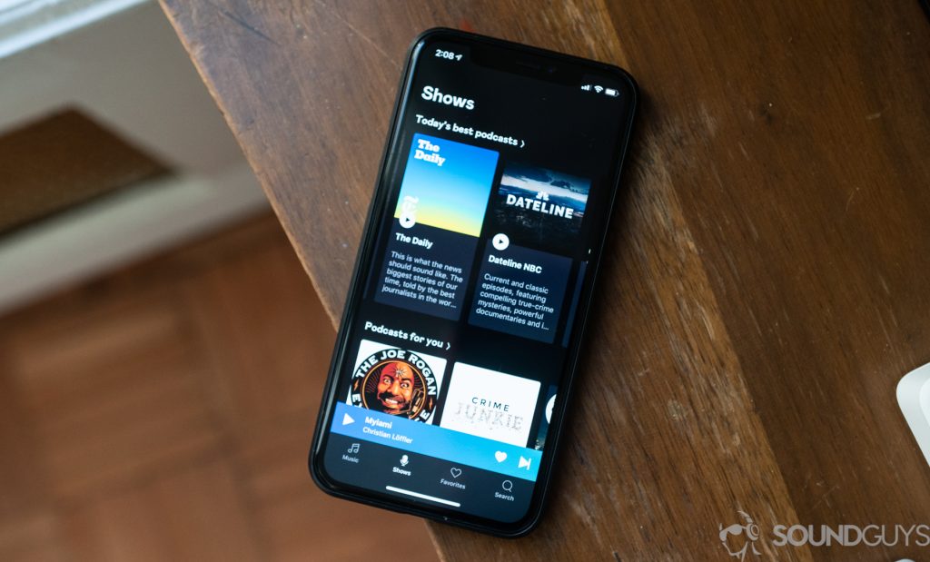 A photo of a smartphone laying on a wooden desk displaying the podcast section of Deezer.