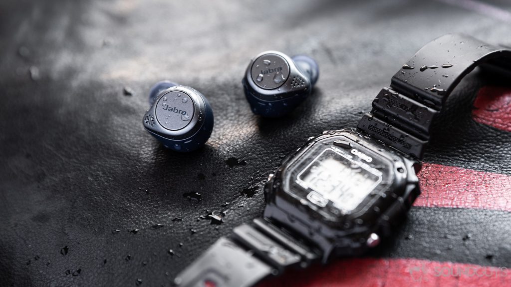 The Jabra Elite Active 75t true wireless workout earbuds (navy) covered in water droplets behind a Casio digital watch.