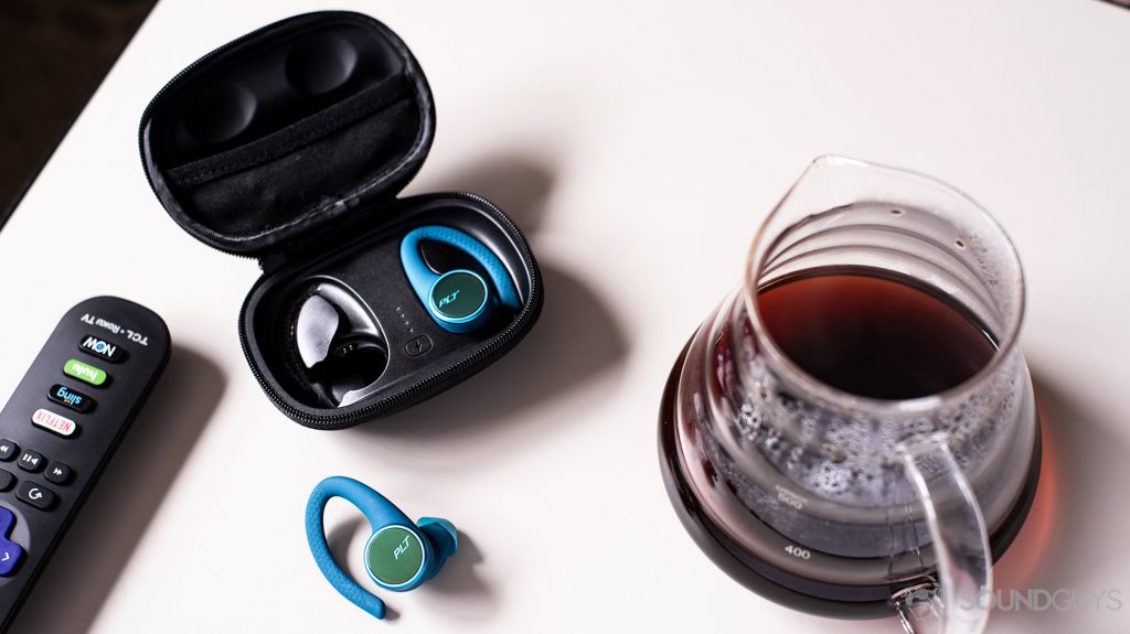 A picture of the Plantronics BackBeat Fit 3200 true wireless workout earbuds in and out of the case next to a carafe of coffee.