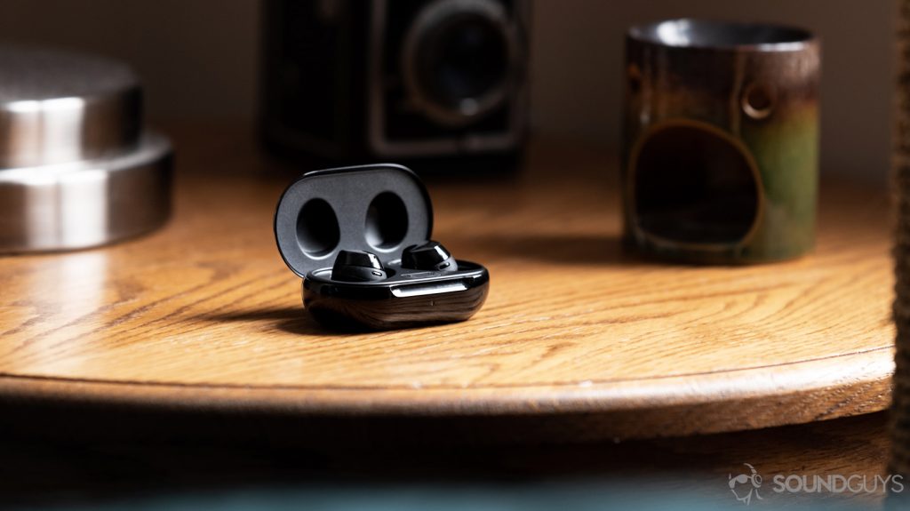 A picture of the Samsung Galaxy Buds Plus true wireless earbuds on a wooden table in front of a vintage camera.