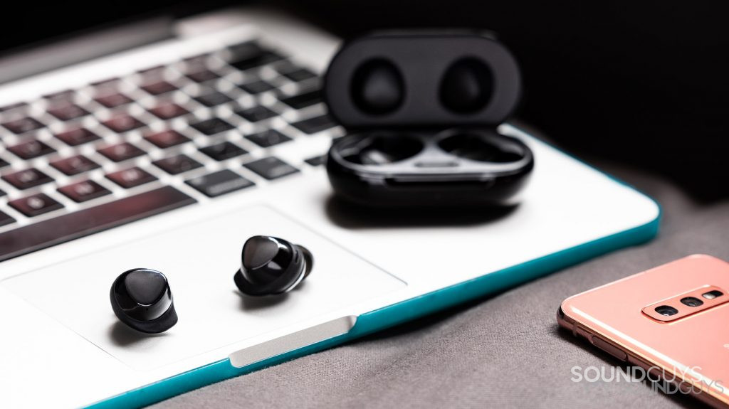 A picture of the Samsung Galaxy Buds Plus true wireless earbuds on top of a Macbook Pro with a Samsung Galaxy S10e in the bottom right corner of the image.