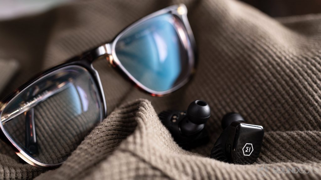 A picture the Master & Dynamic MW07 Go true wireless earbuds in front of Warby Parker tortoise shell glasses.
