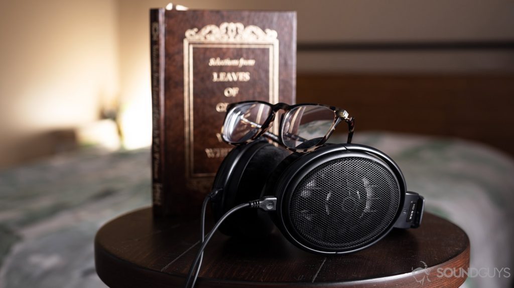 A picture of headphones with glasses on top of the Masdrop x Sennheiser HD 6XX open-back headphones on a stool in front of a book and bed.