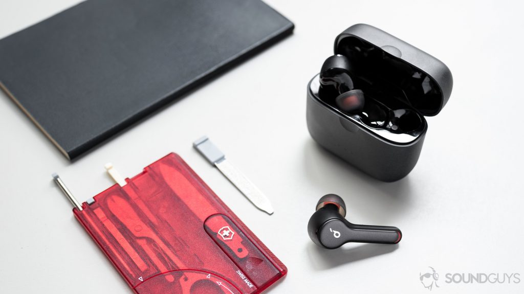 A photo of the Anker SoundCore Liberty Air 2 true wireless earbuds with one earbud int eh case and the other outside of it on white table next to a Swiss Army multitool card in red.