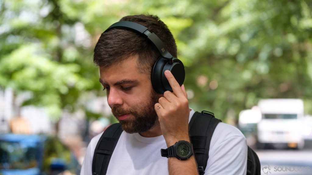 A picture of a man rotating the noise cancelling ring on the Microsoft Surface Headphones 2 in front of trees