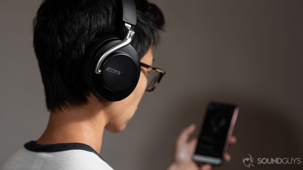 A picture of a woman wearing the Shure AONIC 50 noise cancelling headphones and using the Shure PlayPlus headphone app.