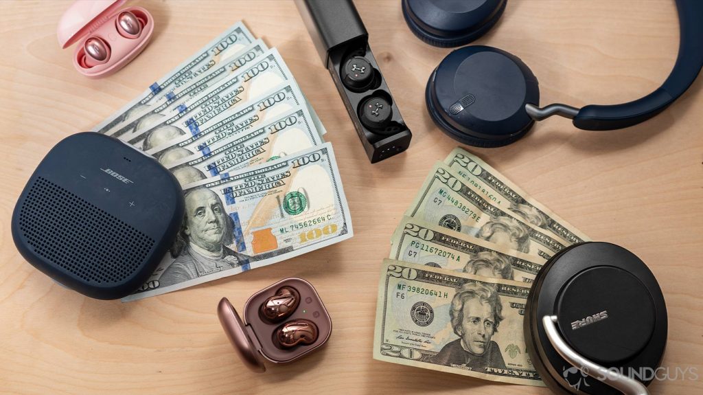 $100 and $20 bills surrounded by wireless audio products like the Bose SoundLink Micro speaker, Samsung Galaxy Buds Live, 1More Colorbuds, Jabra Elite 45h, JBL True Wireless Flash X, and Shure AONIC 50.