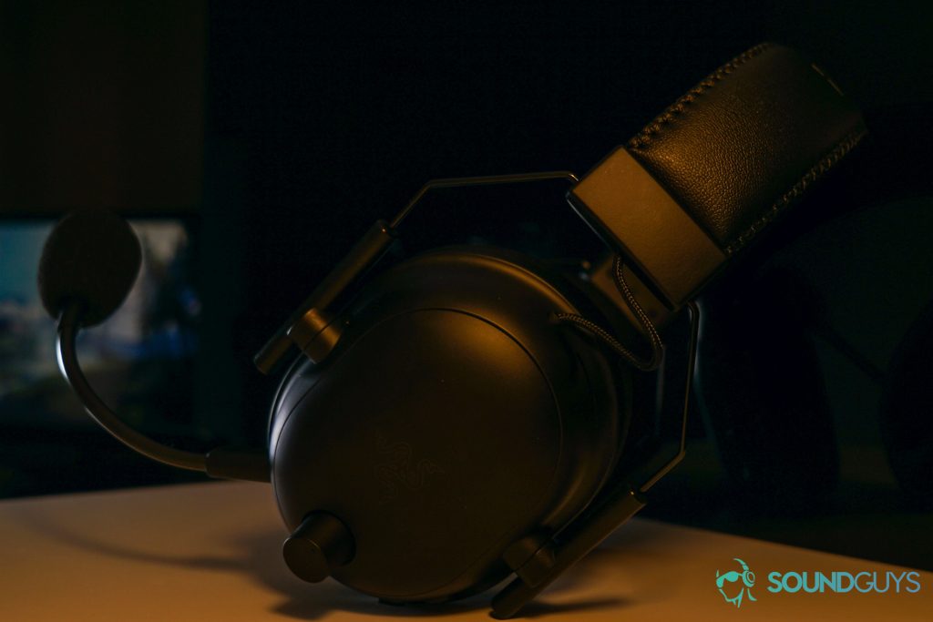 The Razer BlackShark V2 Pro gaming headset sits on a white shelf in front of a reflective black surface with a monitor displaying a Windows 10 desktop in the reflection.