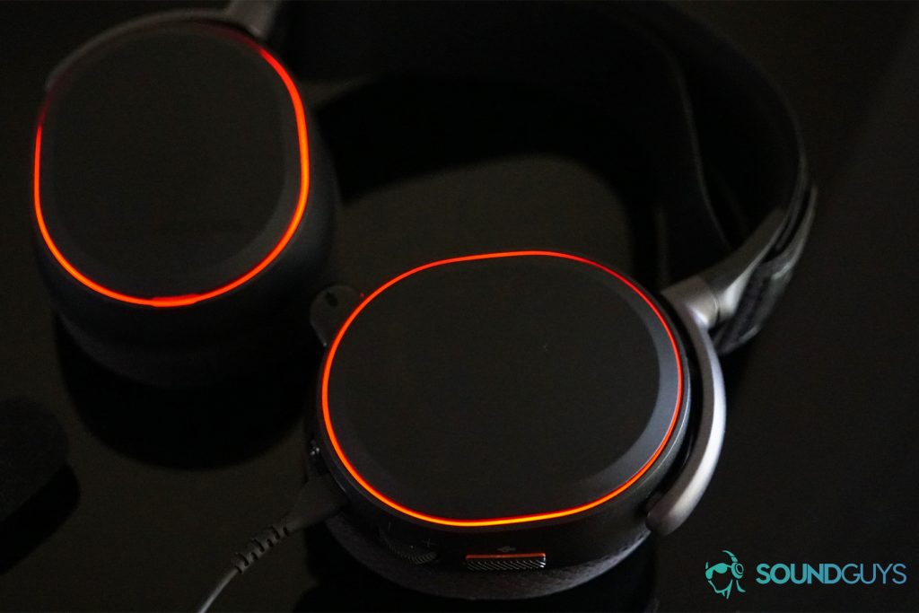 The Arctis Pro lays flat on a black reflective surface with its LED lights glowing orange.