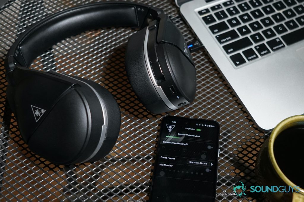 The Turtle Beach Stealth 700 Gen 2 gaming headset sits on a table connected to a Google Pixel 4a via Bluetooth and a MacBook Pro using its USB dongle, next to a cup of coffee.