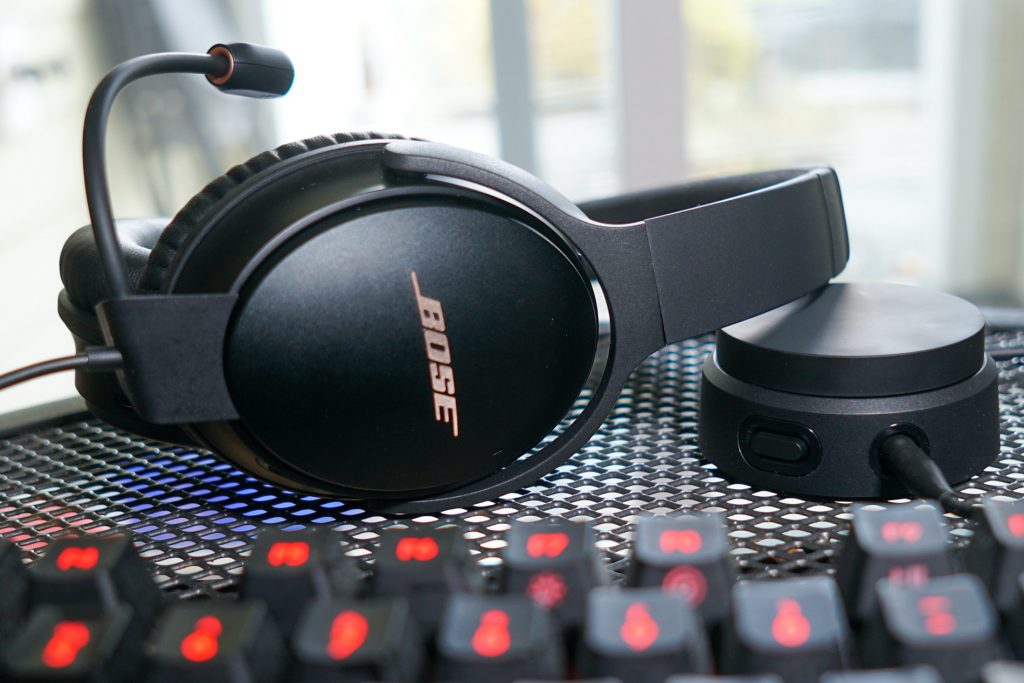 The Bose QuietComfort 35 II Gaming Headset lays on a metal table next to its volume dial and a Logitech G413 Carbon mechanical gaming keyboard.