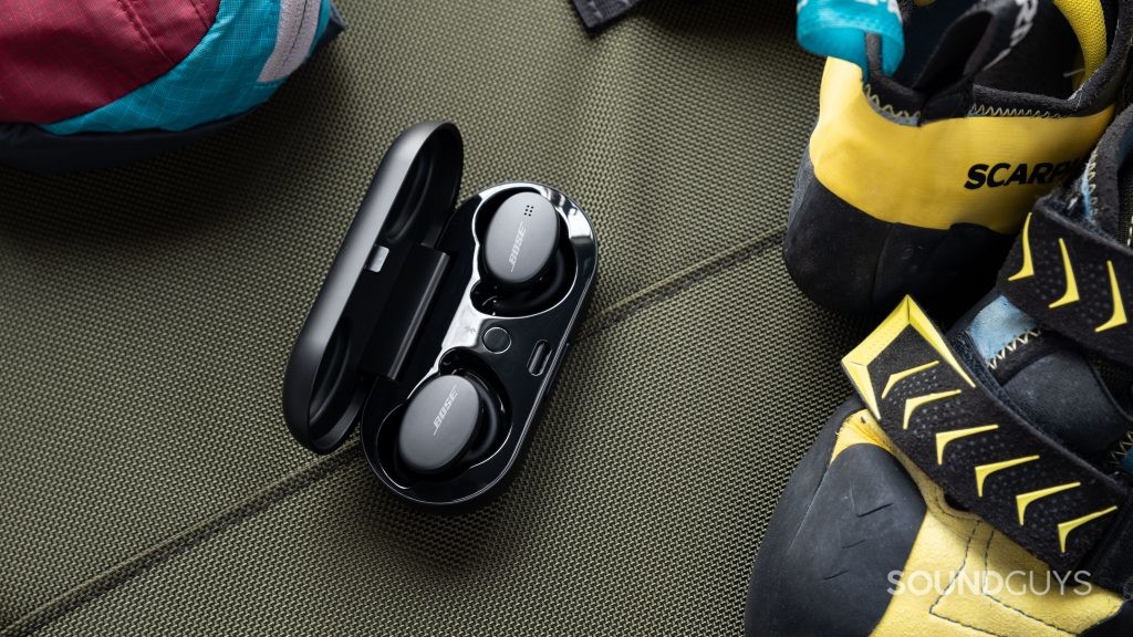 The Bose Sport Earbuds true wireless workout earbuds in the charging case, adjacent to a pair of yellow rock-climbing shoes.