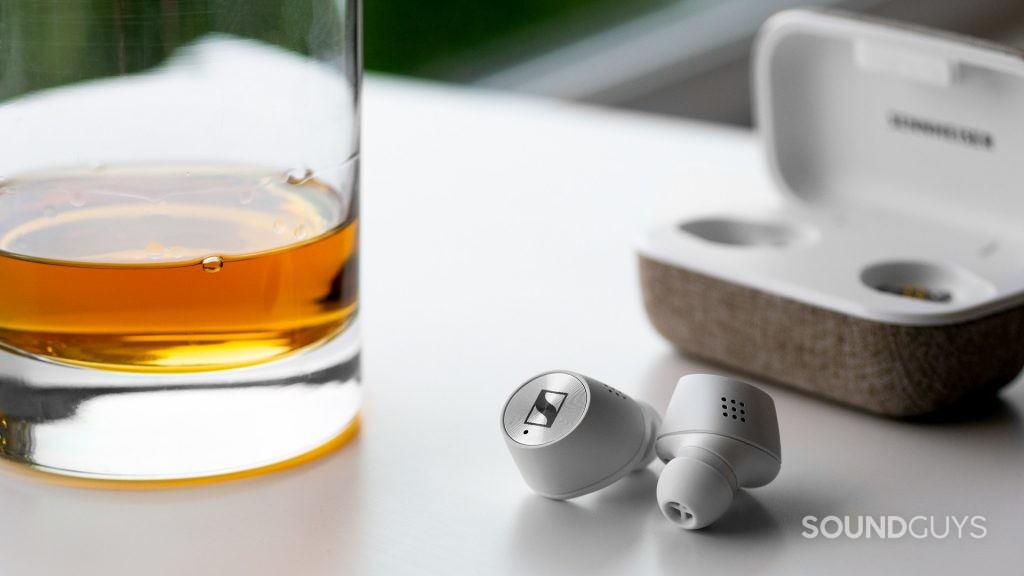 A photo of the Sennheiser Momentum True Wireless 2.0 on a white table next to a glass of whiskey.
