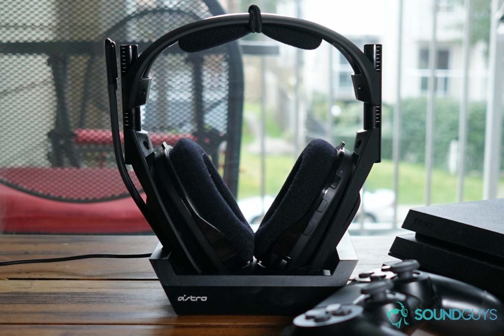 The Astro Gaming A50 Wireless siting in its dock on a wooden table, next to a Playstation 4 and Dualshock controller.