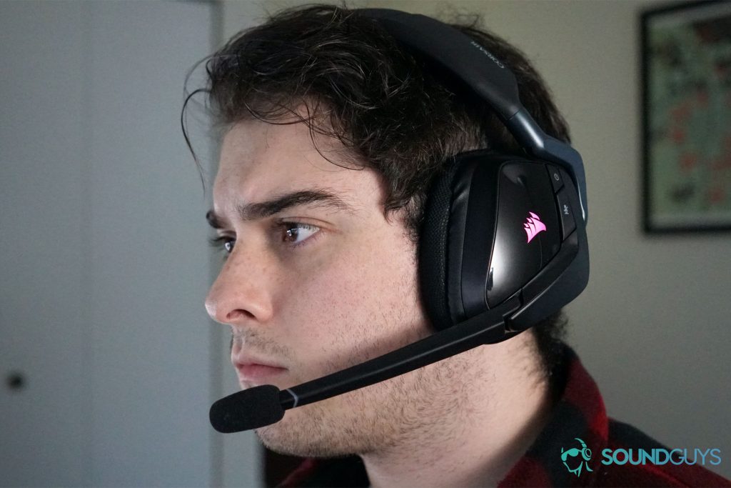 A man wears the Corsair Void RGB Elite Wireless gaming headset with posters in the background.