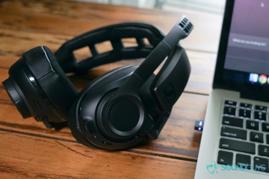 The Sennheiser GSP 670 gaming headset sits on a wooden table next to a MacBook Pro with the headset's USB dongle plugged in.