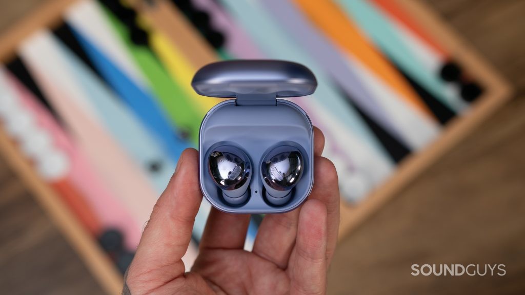 Man holding open case of Samsung Galaxy Buds Pro in hand over colorful game.