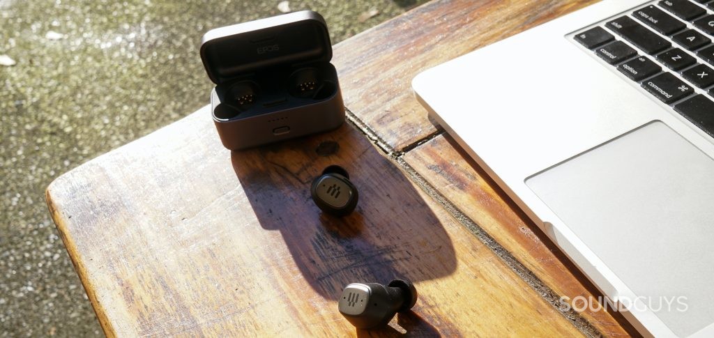 The EPOS GTW 270 Hybrid true wireless earbuds sit next to an Apple MacBook Pro outside in the sunlight, in front of the earbuds charging case.