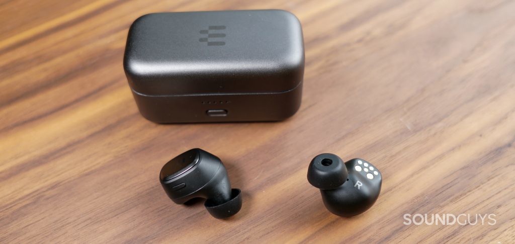 The EPOS GTW 270 Hybrid true wireless earbuds sit on a wooden table in front of their charging case.