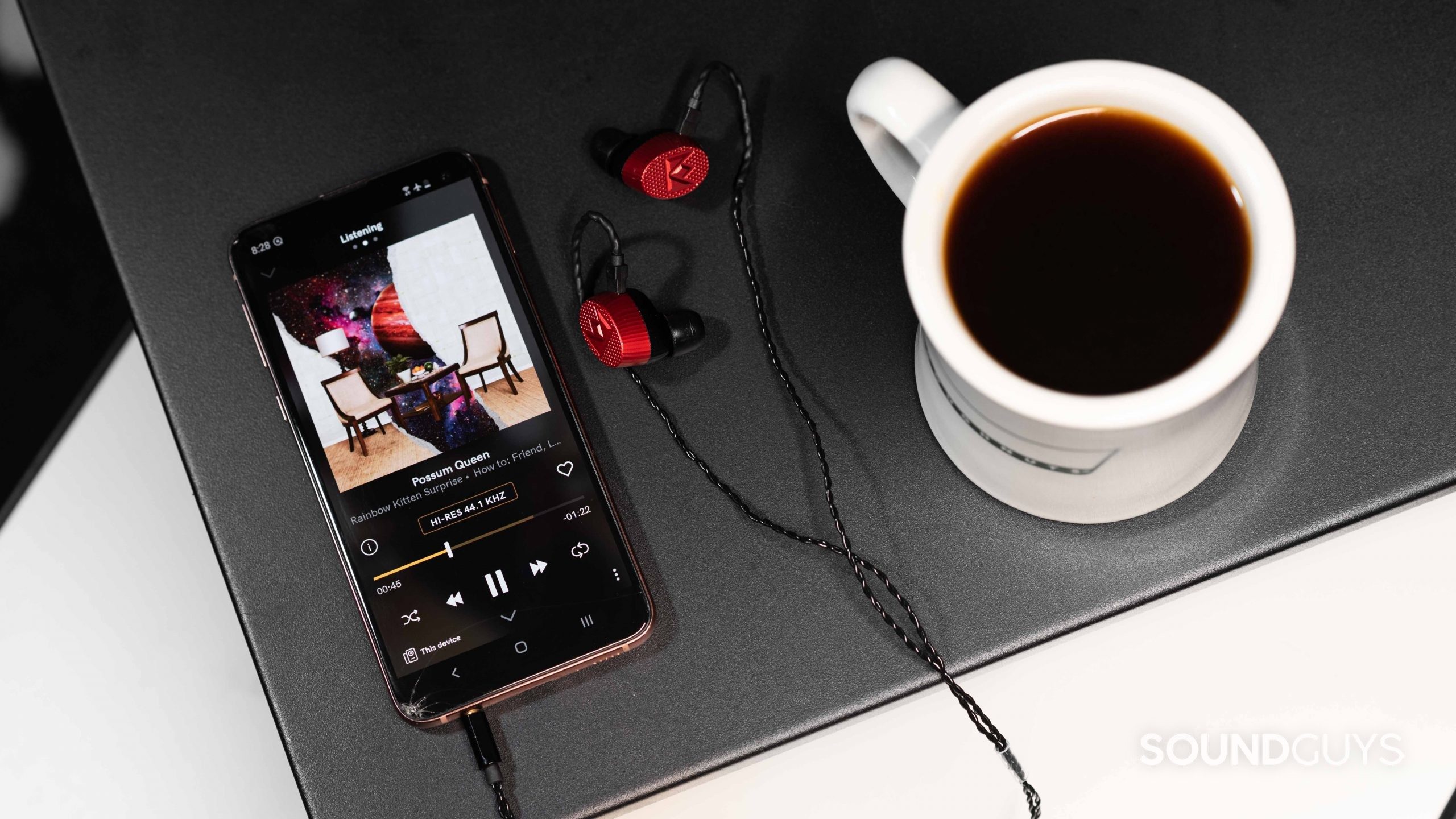 Tab Listening pada aplikasi layanan streaming musik Qobuz terbuka di smartphone Samsung Galaxy S10e di sebelah sepasang Massdrop x Noble Kaiser 10 IEM dan secangkir kopi.