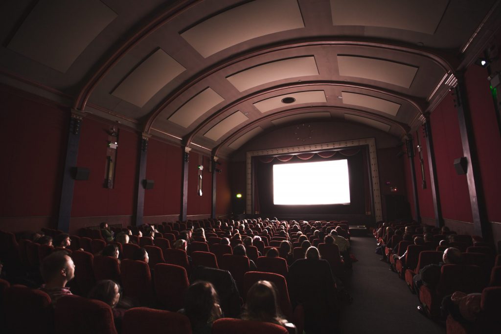 pessoas assistindo a uma tela de cinema vista de trás do Teatro