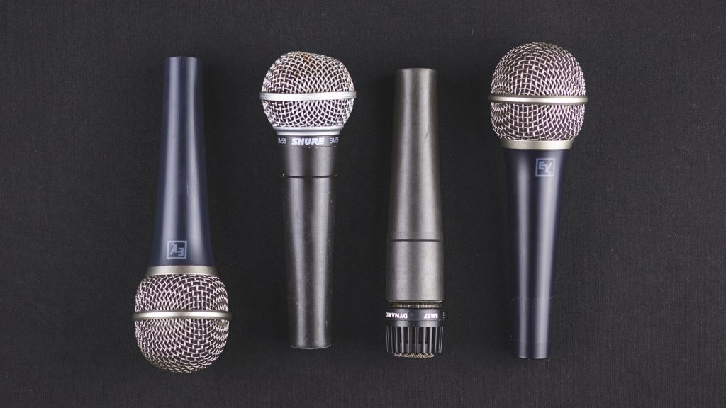 Four handheld cardioid microphones on a black background.