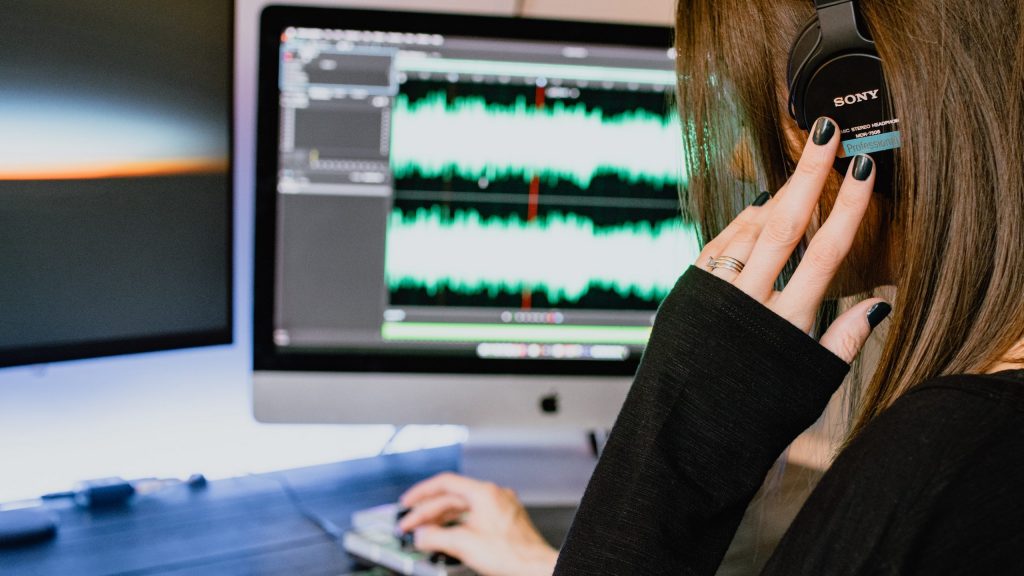 A woman editing audio in a DAW monitors over headphones.