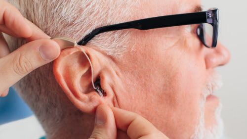 Woman putting a hearing aid into a man's right ear.