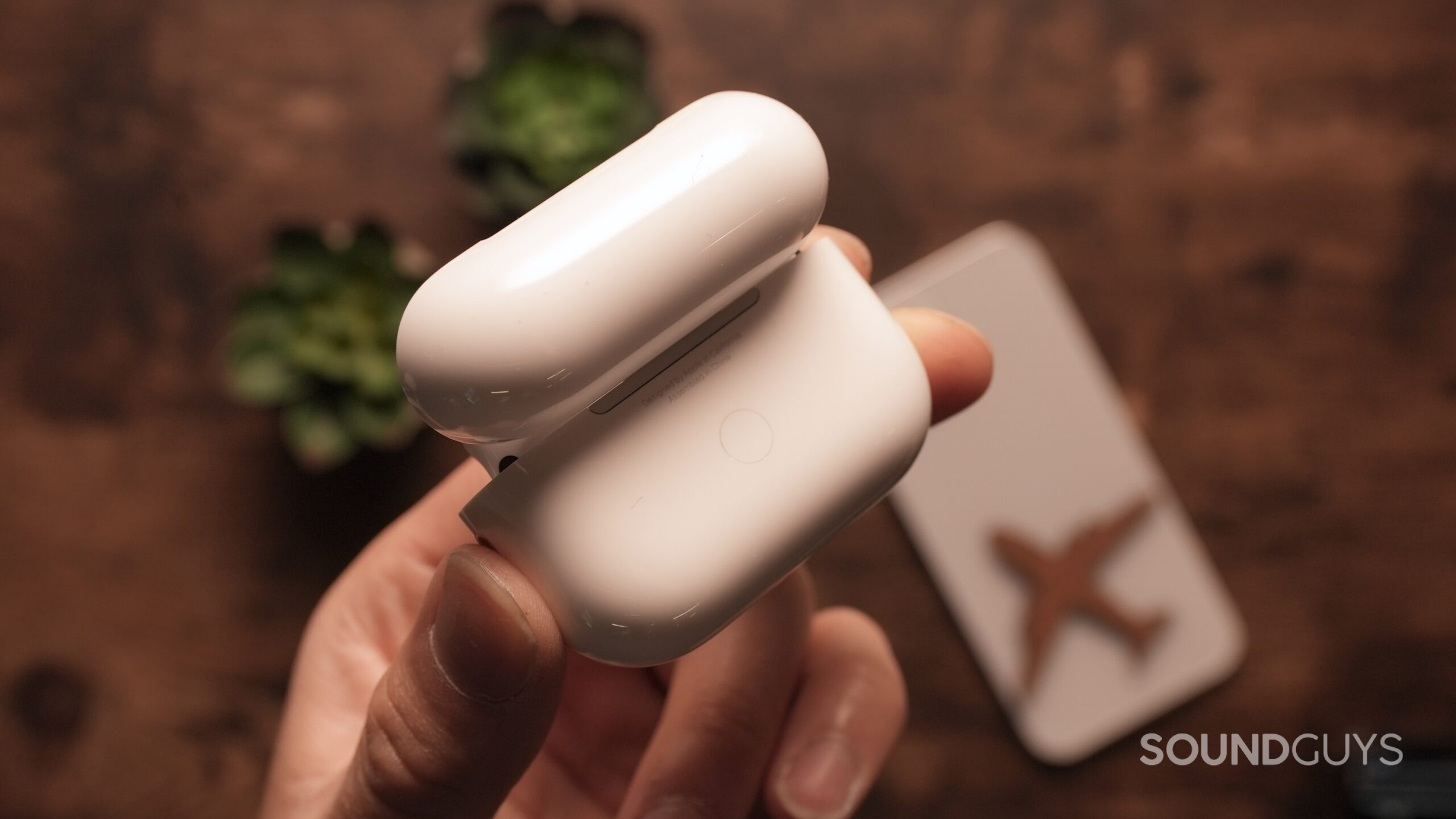 A hand holds the AirPods Pro in their case, open and showing the rear reset button.